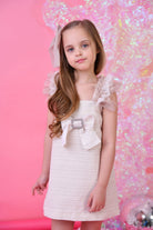 Young girl in glitter tulle dress with ruffled shoulders and crystal bow on pink background