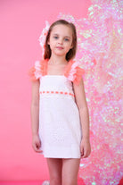 Young girl in white eyelet dress with neon coral tulle sleeves and pink hair accessory, pink background
