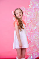 Smiling girl in white eyelet dress with neon pink tulle sleeves, long wavy hair, pink backdrop
