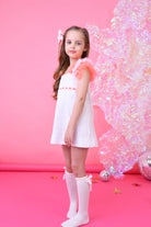 Young girl in white eyelet dress with pink tulle sleeves and knee-high socks on pink background