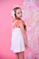 Young girl wearing a white eyelet and pink neon tulle dress with lace hair accessory on pink background