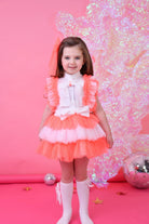 Little girl in a neon coral and white ruffled tulle skirt set with white bow blouse on pink background