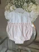 Baby girl's pink and white romper with ruffle sleeves displayed on hanger with white flowers backdrop