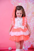 Little girl in neon orange and white tulle skirt dress with bows on pink background
