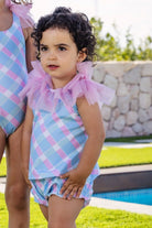 Toddler girl wearing pastel plaid swimsuit with pink tulle ruffles, standing by pool outdoors