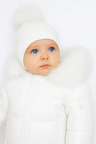 Baby with blue eyes wearing white winter jacket with fur collar and white knit hat with pompom