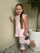 Young girl wearing pink and white striped ruffled pajama set with bow patterns indoors