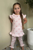 Young girl wearing pink and white striped loungewear set with bow print and ruffle details indoors
