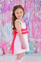 Young girl in pink dress with red ruffled sash posing against colorful pastel backdrop