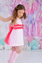 Young girl in pink dress with red sash and pink knee-high socks with bows, colorful festive background